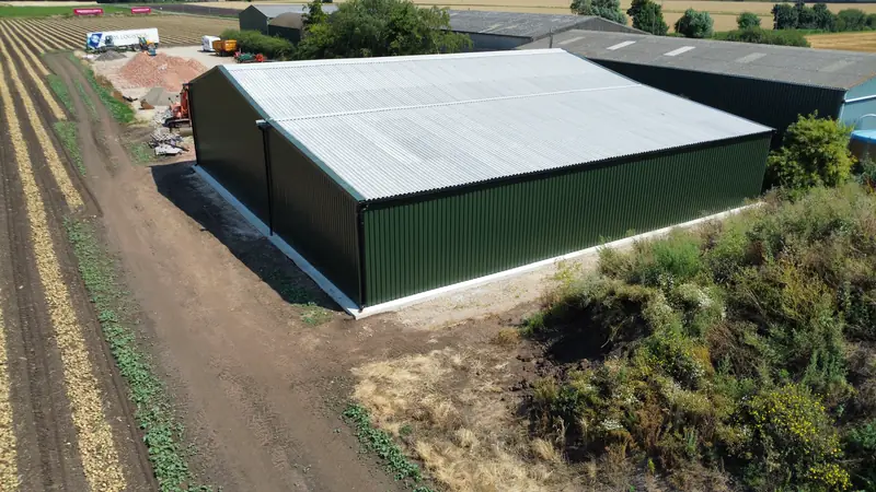 New green steel agricultural building with juniper cladding and a corrugated roof beside farmland
