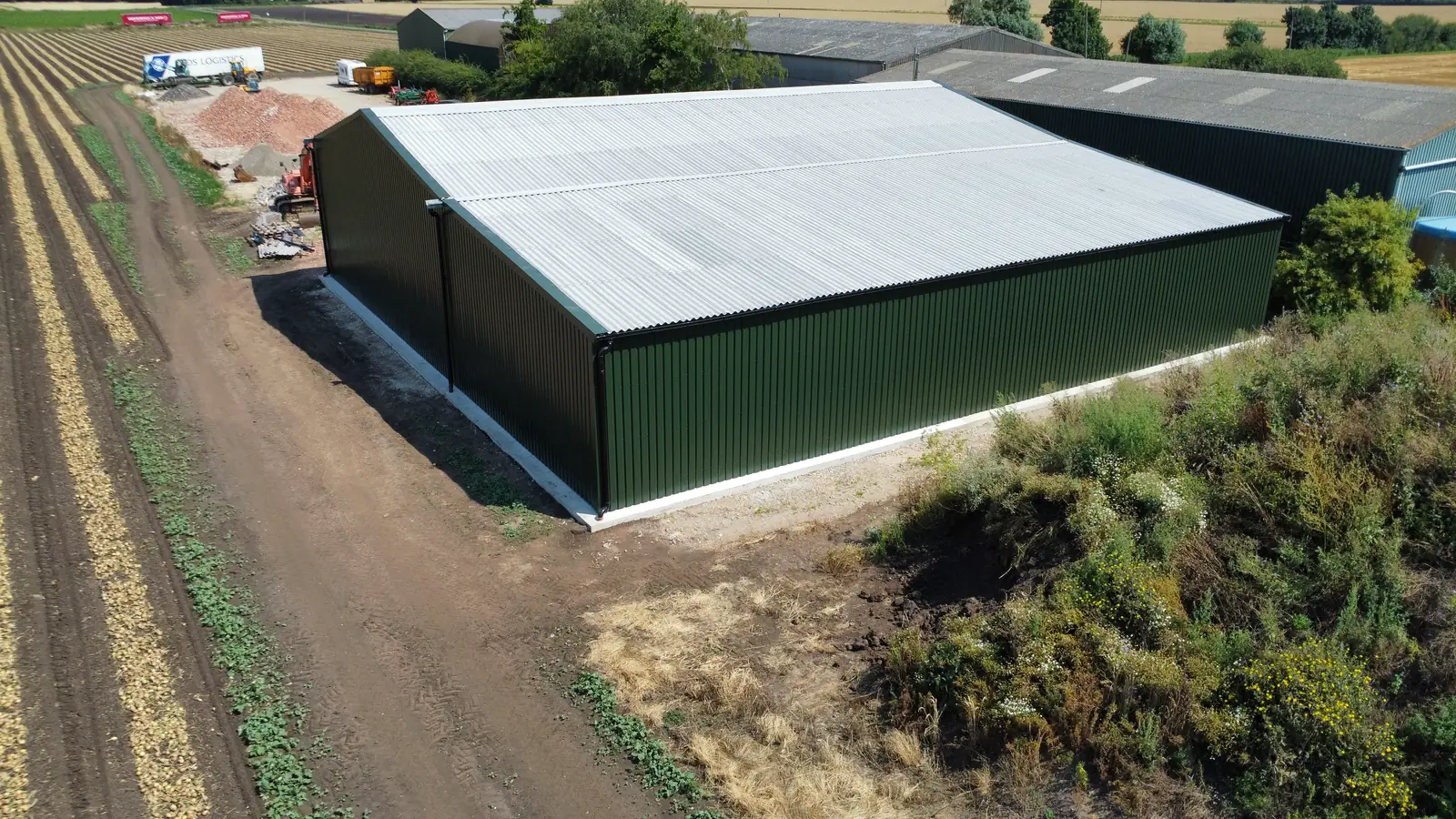 New green steel agricultural building with cladding and a corrugated roof beside farmland