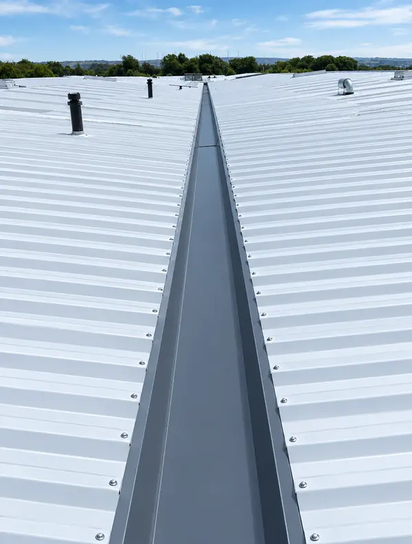 Dark grey lined valley gutter running between two pitches of a white metal roof